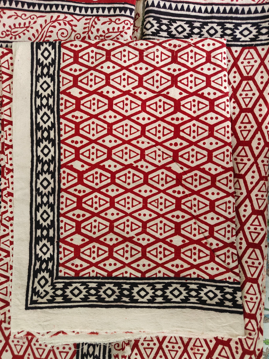 Close-up of a red and white geometric patterned fabric with black accents. Handmade Bagh block print in traditional offwhite with geometric block madder red pattern double bedsheet with pillow cover  
