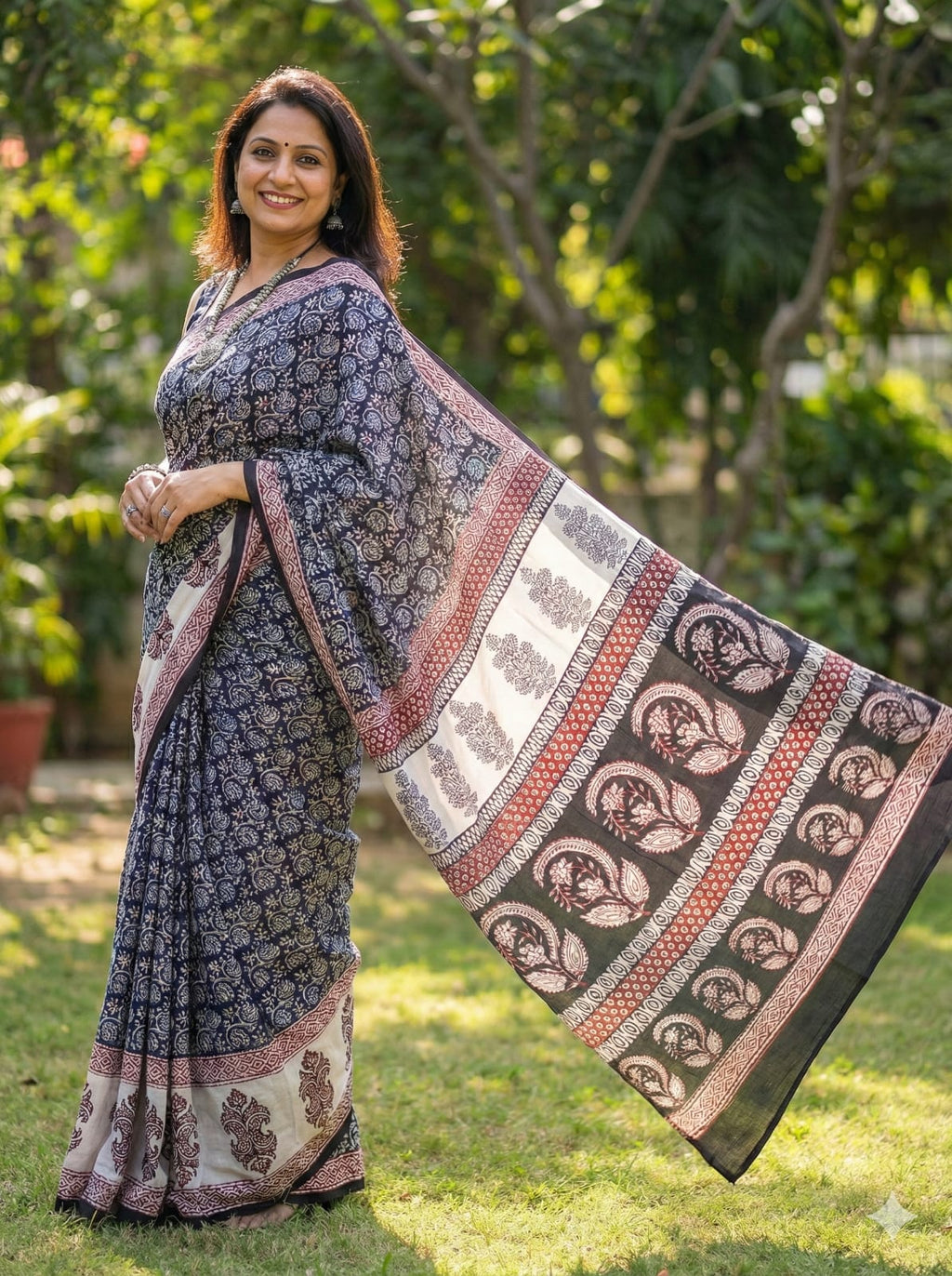 Woman wearing a traditional  Artisan-made saree with a Bagh Block design, standing outdoors with greenery in the background.